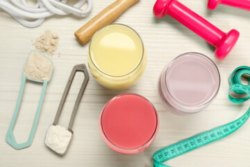Naklejka premium Tasty shakes, sports equipment, measuring tape and different powders on wooden table, flat lay. Weight loss