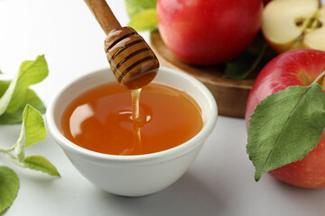 Dripping sweet honey from dipper into bowl and fresh apples on white table, closeup