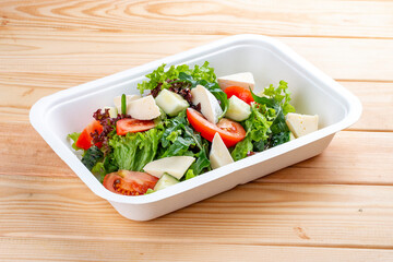 French salad with Camembert cheese. Healthy diet. Takeaway food. Ecological packaging. On a wooden background.
