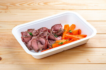 Veal sous vide with juicy carrots. Healthy diet. Takeaway food. Eco packaging. On a wooden background.