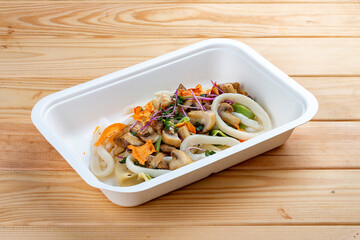 Squid with vegetables in Teriyaki sauce. Healthy diet. Takeaway food. Eco packaging. On a wooden background.