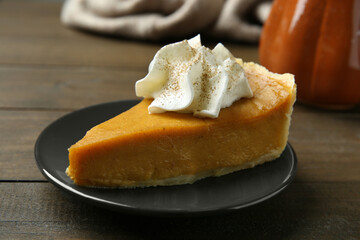 Piece of delicious pumpkin pie with whipped cream on wooden table, closeup