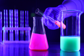 Scientist pouring luminous liquid into laboratory glassware at table, selective focus