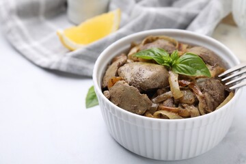 Delicious fried chicken liver with onion and basil in bowl on white table, closeup. Space for text