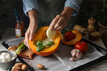Woman stuffing pumpkin with vegetables at table, closeup