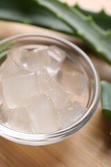 Aloe vera gel and slices of plant on wooden table, closeup