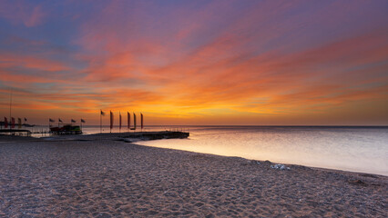 Rhodes island pebble beach, pier with flags and beautiful sunrise with dramatic sky with clouds.