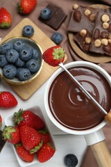 Fondue pot with chocolate, different berries and fork on white wooden table, flat lay