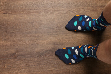 Man in stylish colorful socks standing on wooden floor, top view. Space for text