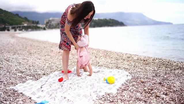 Mom swings upside down a little girl standing on a blanket on the beach. High quality 4k footage
