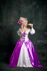 Fototapeta na wymiar Full-length portrait of young attractive woman in dress with corset eating delicious piece of pizza against vintage dark background.