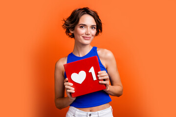 Photo of pretty adorable girl dressed blue top smiling holding feedback heart card isolated orange color background