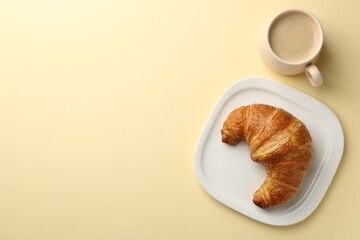 Delicious fresh croissant and cup of coffee on beige table, flat lay. Space for text