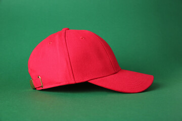 Stylish red baseball cap on green background
