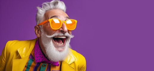 Portrait of cheerful elderly gray-haired bearded grandfather in funny sunglasses and bright extravagant clothes on plain purple background. Retired hipster, seniors party, carnival