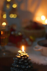 Cup of tea or coffee, glass of wine or juice, bowl of cookies, organic pomegranate, fluffy blanket, pine cones, various Christmas decorations and lit candles on the table. Christmas hygge concept.