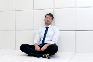 Sad and frustrated businessman in formal wear sitting in a white room in a mental hospital