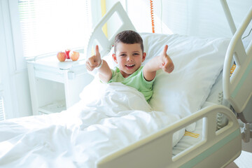 Portrait of a smiling European seven year old boy in a light green T-shirt lying on the bed in a...