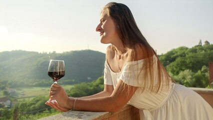 Young woman, her glass of red wine gracefully held, set against the backdrop of a mountain sunset...