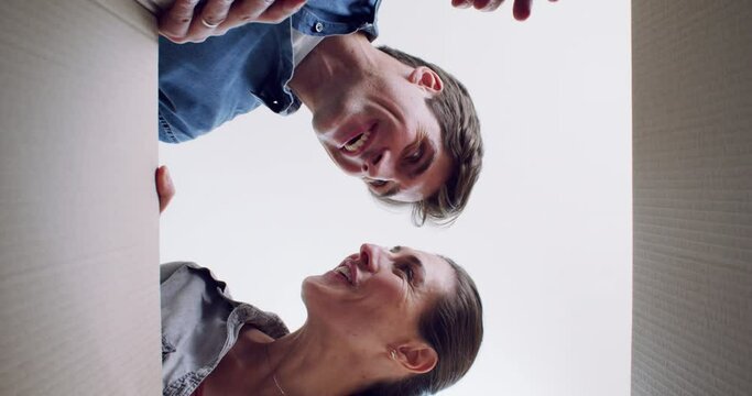 Face, wow and a couple opening a box together in their new home on moving day from below. Portrait, smile or happy with a young man and woman in their apartment for real estate or property investment