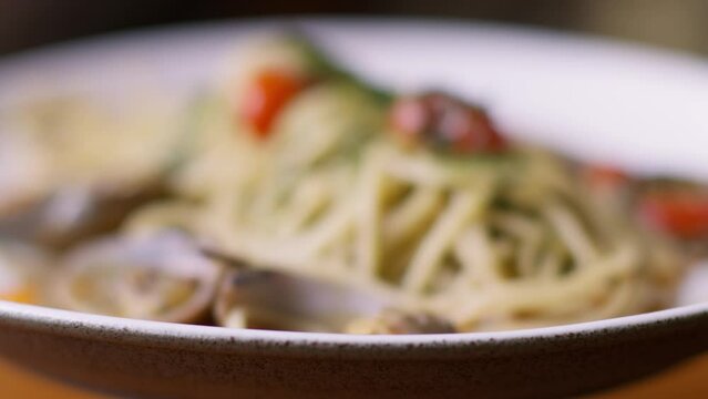 A serving of long spaghetti pasta in a large light plate, sprinkled with herbs, tomatoes and vongole. A dream Italian lunch somewhere in a cafe in Rome or Milan. Spaghetti with seafood and shells