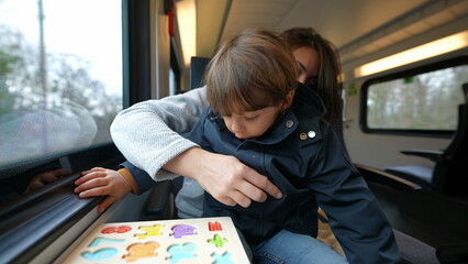 Mother holding her son while traveling by train in daily commute, parent multi-tasking on the go