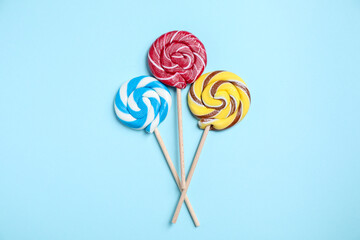 Sticks with colorful lollipops on light blue background, flat lay