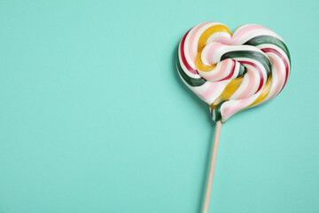 Stick with heart shaped lollipop on turquoise background, top view. Space for text