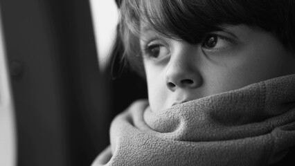 Monochromatic close-up face of a pensive child wearing scarf gazing out in deep mental reflection,...