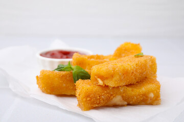 Tasty fried mozzarella sticks with basil leaves on white table, closeup