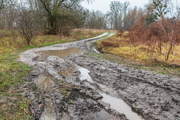 Dirty rural country road with puddles and mud after heavy rain on an autumn day