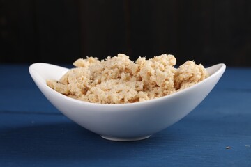 Bowl of tasty prepared horseradish on blue wooden table, closeup