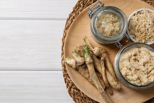 Platter with tasty prepared horseradish and roots on white wooden table, top view. Space for text
