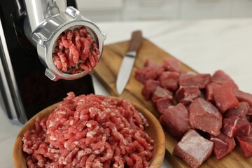 Electric meat grinder with beef on white table indoors