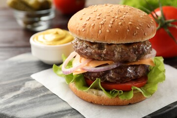 Tasty hamburger with patties, cheese and vegetables on board, closeup