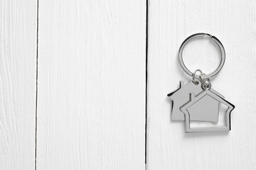Metal keychain in shape of houses on white wooden table, top view. Space for text
