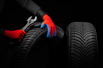 Winter car tires service and hands of mechanic with wrench, screwdriver on black background.