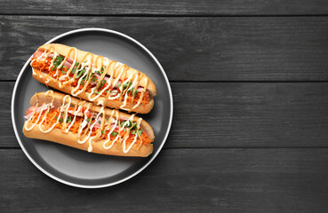 Delicious hot dogs with bacon, carrot and parsley on black wooden table, top view. Space for text