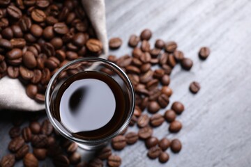 Glass of coffee liqueur and beans on grey table, top view. Space for text