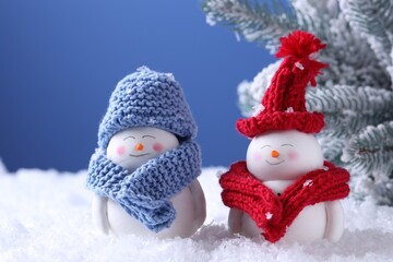 Cute decorative snowmen and fir tree on artificial snow against light blue background, closeup