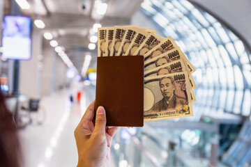 Hand holding a passport with ten thousand Japanese yen bills at the airport