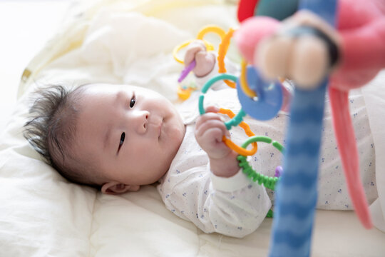 A baby who is just a few days old is lying next to a sunny window and playing with toys