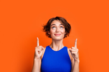 Photo of excited dreamy girl dressed blue top looking showing two fingers up empty space isolated orange color background