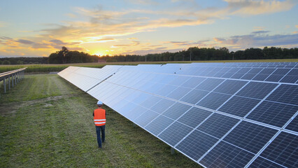 Aerial drone view following a Technician at work on a solar farm, during sunset