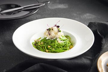 Elegantly plated pesto spaghetti with creamy stracciatella cheese and toasted pine nuts, served in a white bowl on a sleek black surface