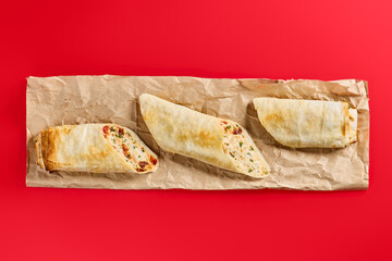 Top view of a Serbian burekas roll, cut open to show a hearty cheese and spinach filling, laid out on crinkled parchment against a red background