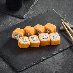 Golden Philadelphia tempura roll filled with salmon, cucumber, and cream cheese, presented on a textured black slate
