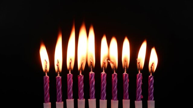 Purple birthday candles burning on black background.