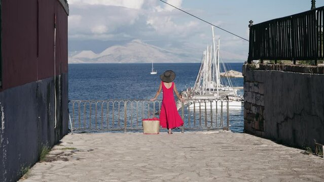 Tourist woman in dred dress enjoy view of the old Venetian fortress and yachts pier of Corfu Island town, Greece
