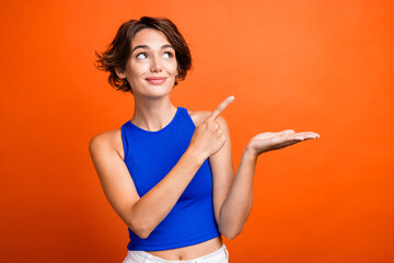 Photo of pretty dreamy girl dressed blue top open mouth looking pointing finger showing arm empty space isolated orange color background